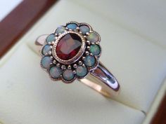 This gorgeous Vintage Inspired Flower Ring has been crafted from 9ct Solid Rose Gold with an oxidised background vintage effect. A bezel set oval cut NATURAL Garnet with surrounding NATURAL Opals brings this ring to life. Notice the stamens that surround the petals of this beautiful ring. This is an elegant Victorian inspired ring which simply looks beautiful on a lady who enjoys wearing fine jewellery from a Vintage era.  THIS VINTAGE INSPIRED GARNET & OPAL RING IS TRULY AN EXQUISITE FINE JEWEL Opal Ring Vintage, Garnet Ring, Funky Jewelry, Garnet Rings, Opal Ring, Multi Stone Ring, Jewelry Inspo, Dream Jewelry, Ring Vintage