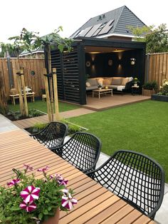 an outdoor living area with wooden tables, chairs and flowers on the grass in front of it