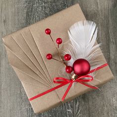 a gift wrapped in brown paper with white feathers and red berries on it next to a christmas ornament