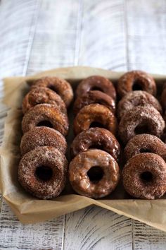 a box filled with lots of donuts on top of a wooden table covered in wax paper