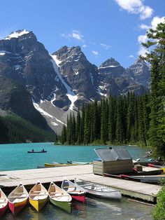 several canoes are tied up to the dock in front of some snow covered mountains