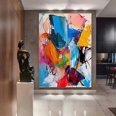 an abstract painting hangs on the wall next to a statue in a modern living room