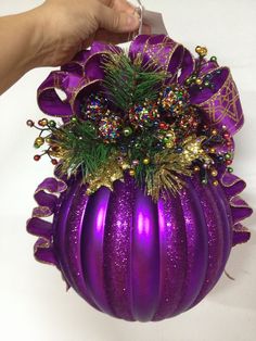 a hand holding a purple christmas ornament with gold and green decorations on it