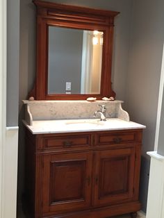 a bathroom with a sink, mirror and wooden cabinetry in it's corner