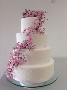 a three tiered white cake with pink flowers on the top and bottom, sitting on a glass table