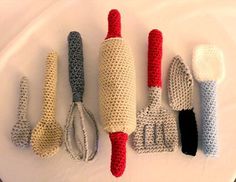 crocheted kitchen utensils are arranged on a white tablecloth with red and blue handles