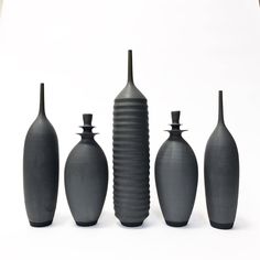 five black vases lined up next to each other on a white surface with no one in the photo