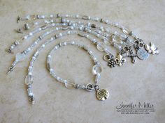 a white beaded necklace with silver charms and flowers on the clasp is laying on a marble surface