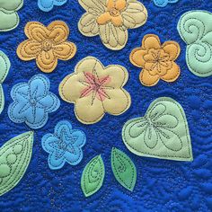 a blue quilt with flowers and leaves on the bottom is stitched in yellow, orange, and green