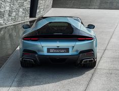 the rear end of a blue sports car parked in front of a building with water