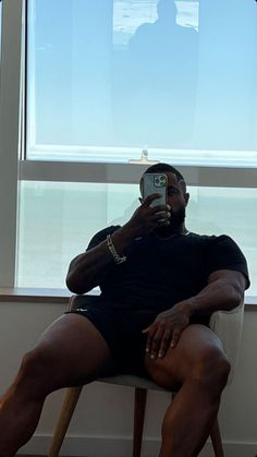 a man sitting in a chair taking a selfie with his cell phone while looking out the window