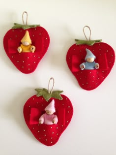 three strawberry shaped ornaments hanging from strings on a white wall with two small gnomes