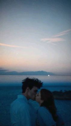 a man and woman kissing on the beach at dusk with an island in the background