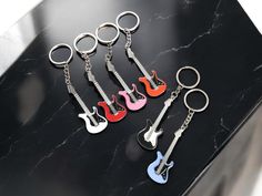 six guitar shaped key chains on a black counter top with one red, one blue and one pink