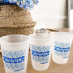 three plastic cups sitting on top of a wooden table next to a basket with flowers