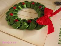 a close up of a christmas wreath on a card with a red ribbon around it