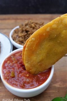 the dipping sauce is being poured into two small white bowls with food in them on a wooden surface