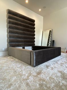 a bed sitting on top of a white carpet covered floor next to a tall mirror