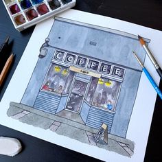 a drawing of a coffee shop on a table next to paintbrushes and watercolors