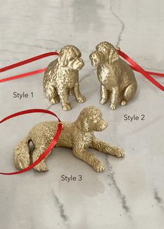 three golden dog ornaments tied together on a marble surface with red ribbon around the dogs