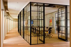 an office with glass walls and wooden floors is pictured in this image from the hallway