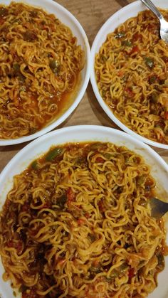 three white bowls filled with noodles and sauce on top of a wooden table next to silverware