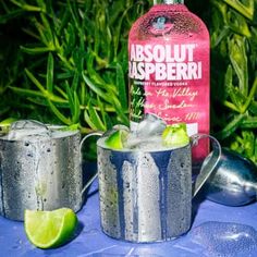 two glasses filled with ice and limes next to a bottle of absolut raspberry