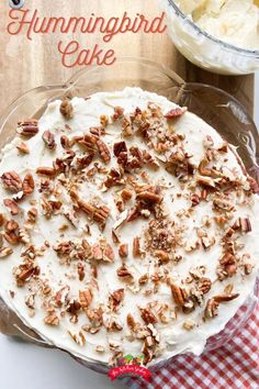 hummingbird cake with white frosting and chopped pecans on top in a glass pie dish