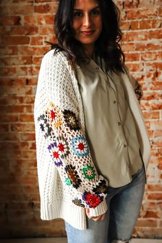 a woman standing in front of a brick wall wearing a white sweater and blue jeans