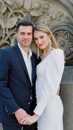 a man and woman standing next to each other in front of a stone wall with carvings on it