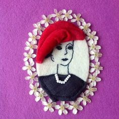 an embroidered brooch with a woman's face in a red beret surrounded by flowers