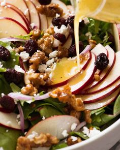 someone pouring dressing onto a salad with apples, walnuts, and cranberries