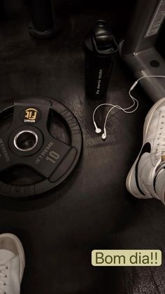 a pair of white sneakers sitting on top of a black floor next to an electronic device