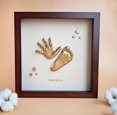 two gold baby hand and foot casts in a shadow box with cotton balls on the floor