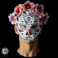 a man wearing a white mask with flowers on his head and the face painted in black