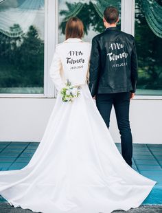 the bride and groom are standing in front of large windows with their back to the camera