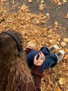 a woman sitting on the ground with her hands in her pockets and two cups of coffee