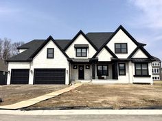 a white brick house with black trim on the roof and two car garages in front