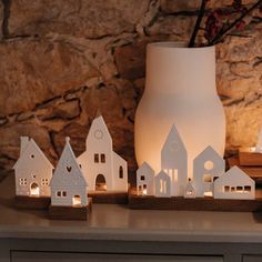 small white houses are lit up on a table next to a vase with flowers in it