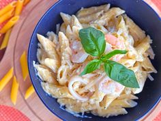 a blue bowl filled with pasta and shrimp on top of a wooden table next to cheese sticks