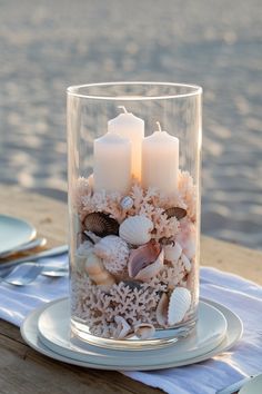 Beach-themed wedding centerpiece with seashells and candles layered in a glass vase, perfect for a coastal wedding. Beach Wedding Centerpieces Diy, Beachy Centerpieces, Nautical Wedding Centerpieces, Beach Theme Wedding Reception, Coastal Wedding Centerpieces, Beach Theme Centerpieces, Budget Friendly Wedding Centerpieces, Affordable Wedding Centerpieces