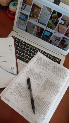 an open laptop computer sitting on top of a wooden desk next to a notebook and pen