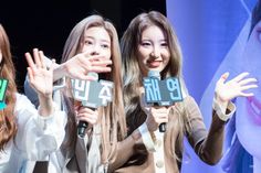 three girls are holding up signs in front of a stage with an advertisement behind them