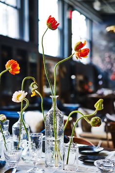 flowers are in vases on a table with glasses and silverware, as well as plates