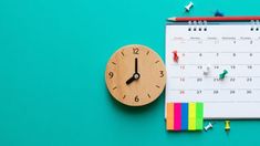 a calendar with pins on it next to a wooden clock and colored pencils,