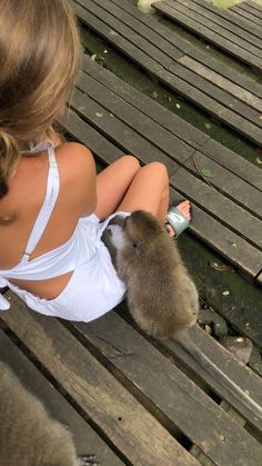 a woman sitting on top of a wooden bench next to a small monkey in her lap