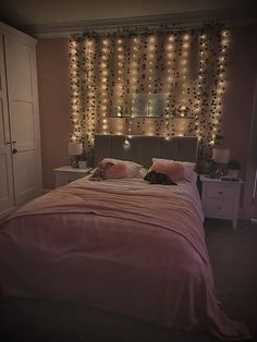 there is a bed with pink sheets and lights on the wall behind it in this bedroom