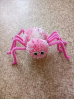 a close up of a pink spider on the ground with eyes and legs made out of pom poms