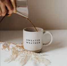 a person pours tea into a coffee mug with the words sweater weather on it