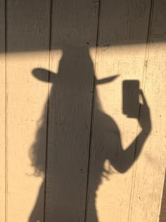 the shadow of a person with a hat on their head and holding a cup in his hand